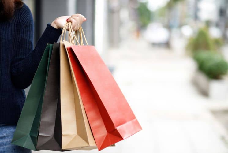 A woman in a blue sweater holding four paper shopping bags of different colors