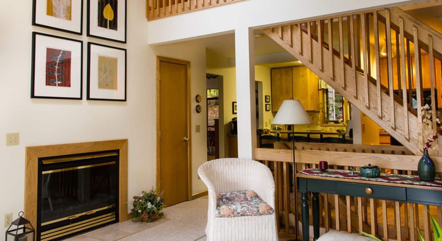 A living room with fireplace, tall ceilings, look through to a kitchen and stairwells with railings going both upstairs and downstairs