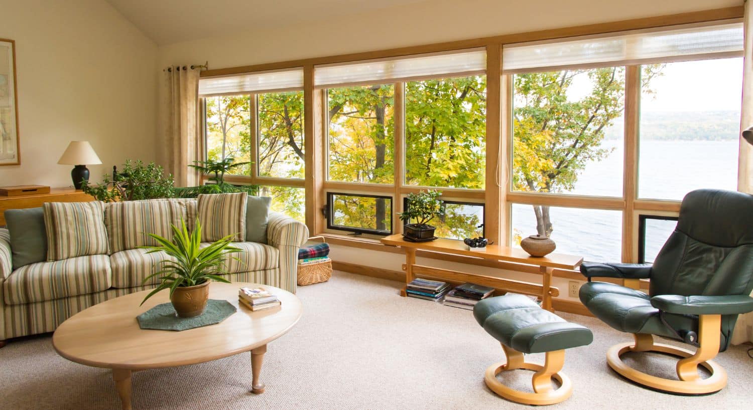 Spacious living room with striped couch, table, chair and wall of windows overlooking a lake