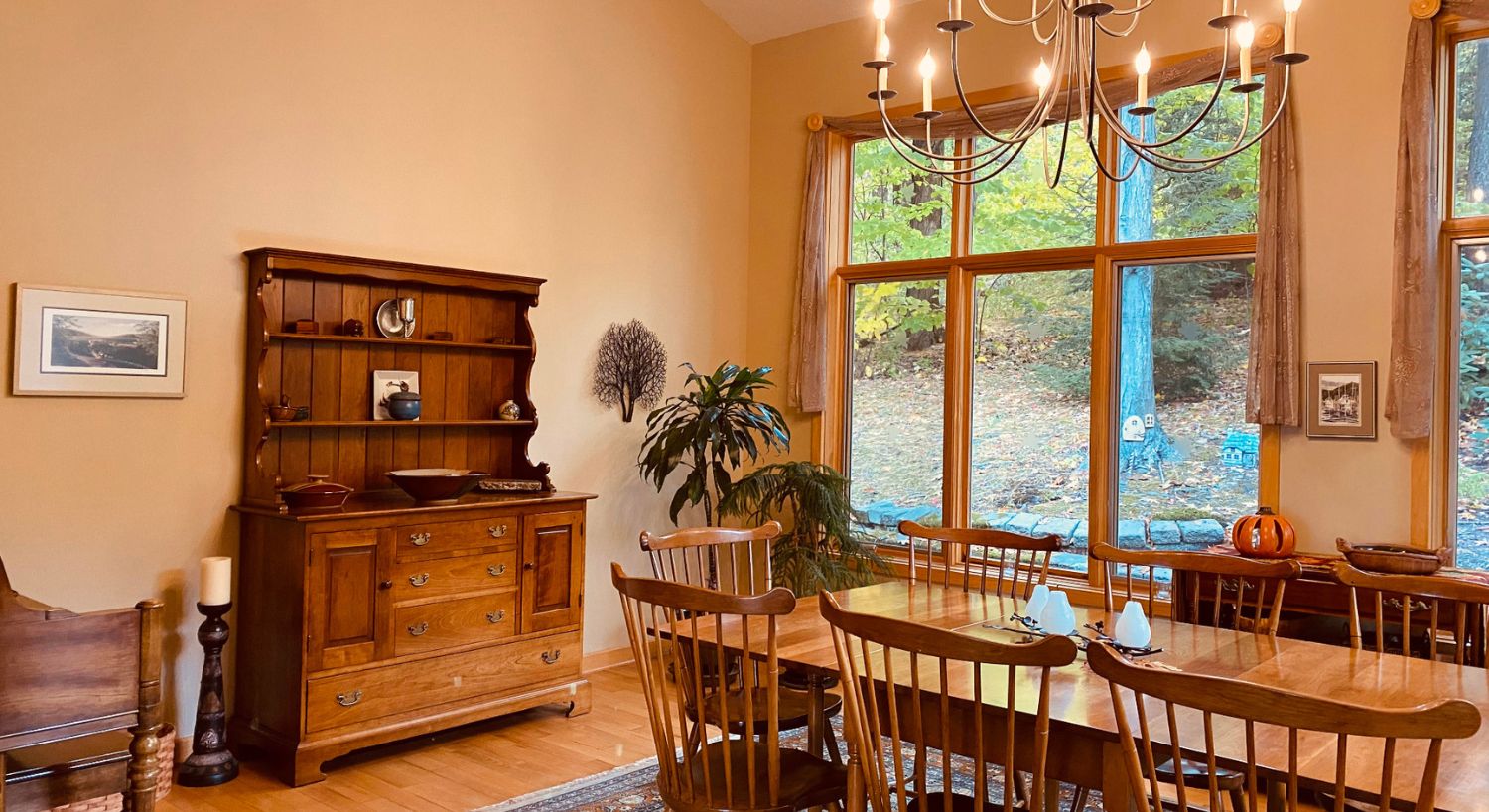 Large and spacious dining room with table and chairs, large hutch, chandelier and tall windows overlooking the woods