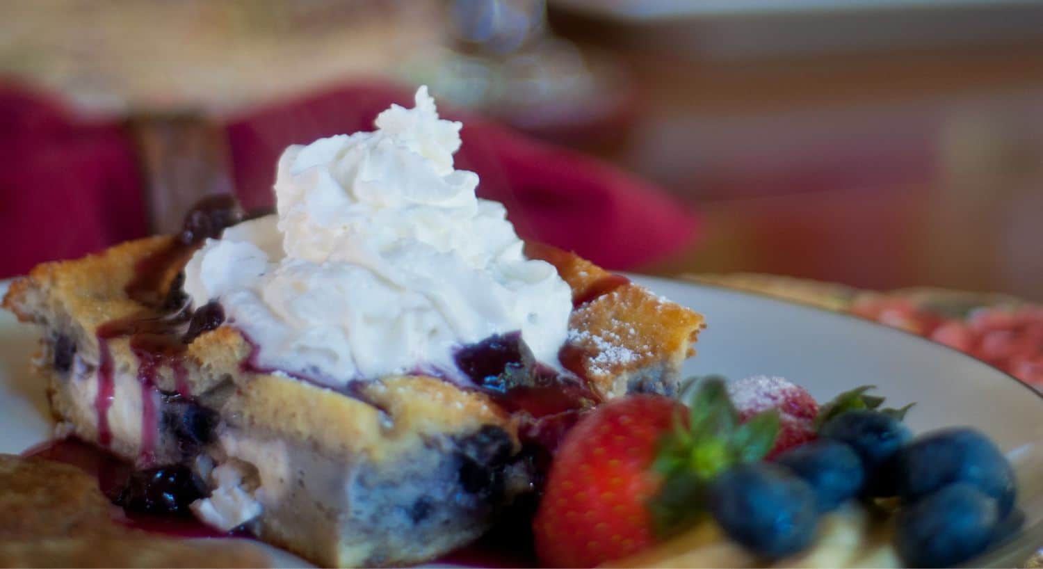 Blueberry breakfast French toast with whipped cream and a side of strawberries and blueberries