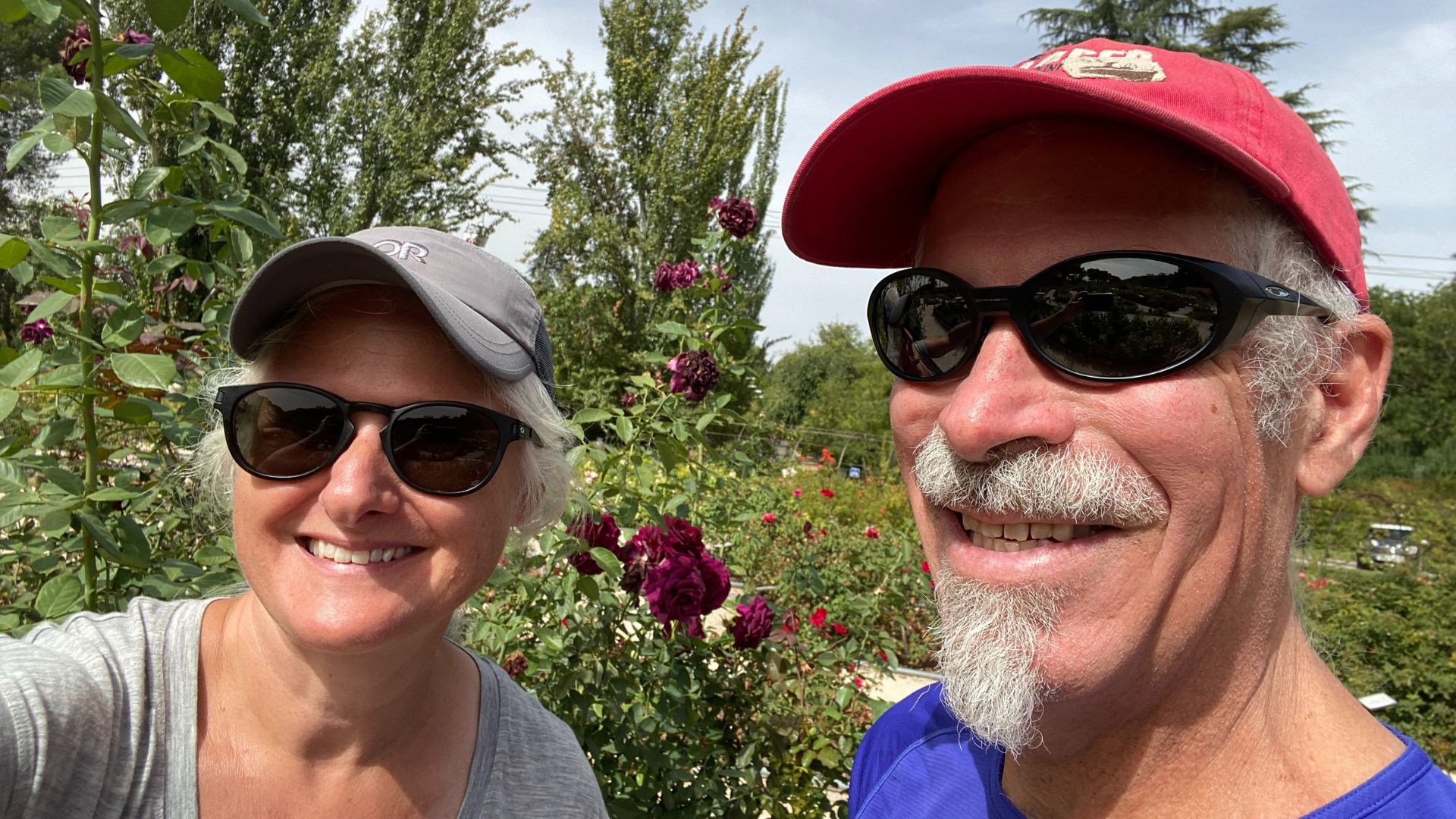 A man and woman, both in baseball caps and sunglasses outside in a garden