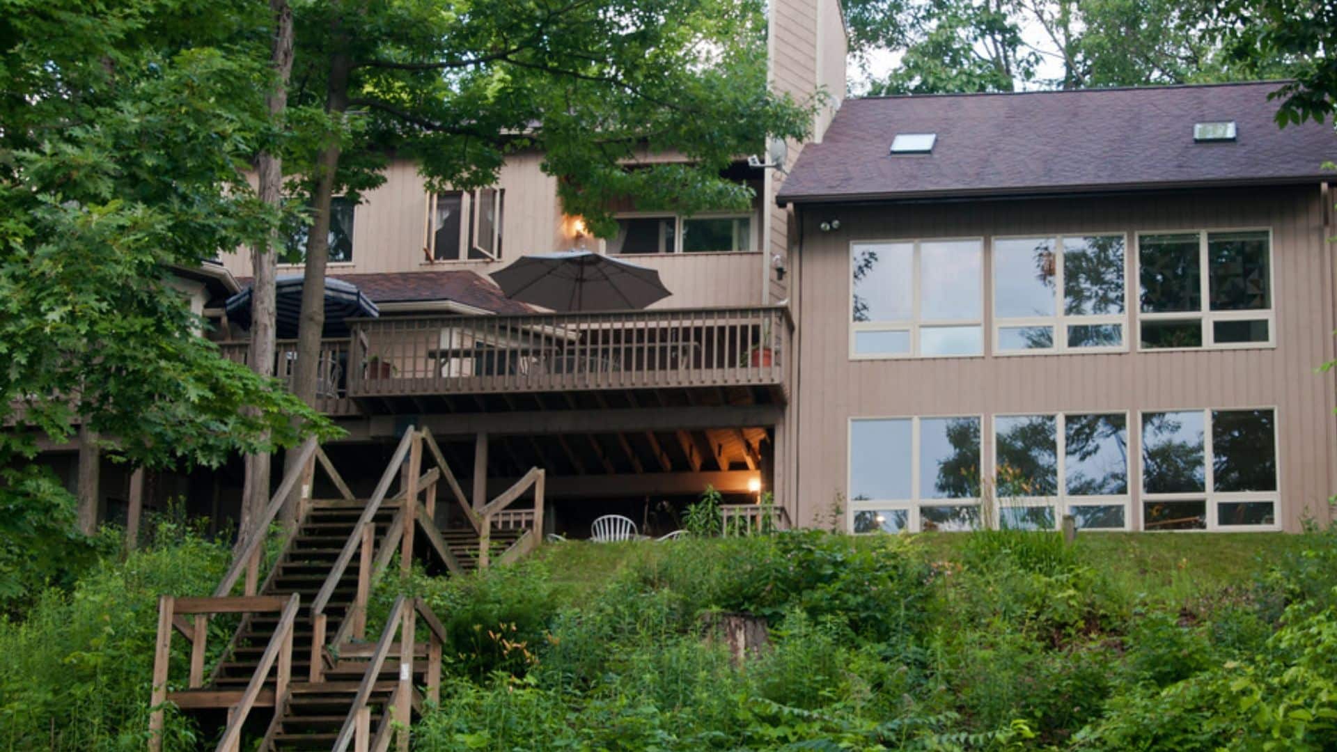 Rear view of a large three story home with outdoor deck, lots of windows and stairs going down to a lake