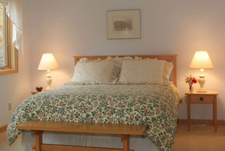 Bedroom with queen bed with a colorful floral quilt, side tables with lamps and window with white curtains