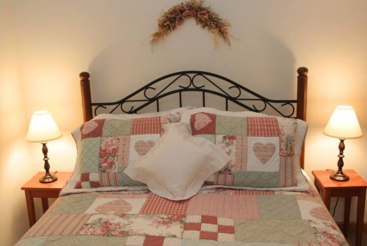 Bedroom with wood and iron bed with colorful patchwork quilt, side tables with lamps and floral swag over the headboard