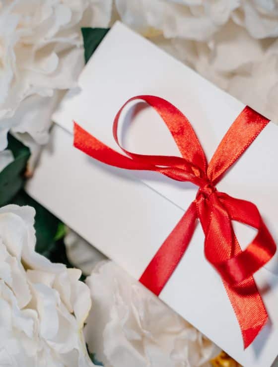 A white envelope tied with a red ribbon sitting on white flowers