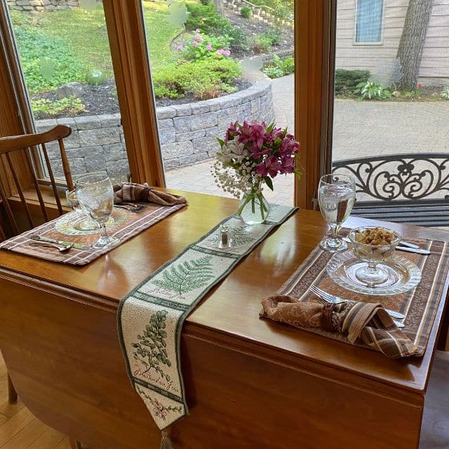 A wood drop leaf table set for breakfast for two next to a large window