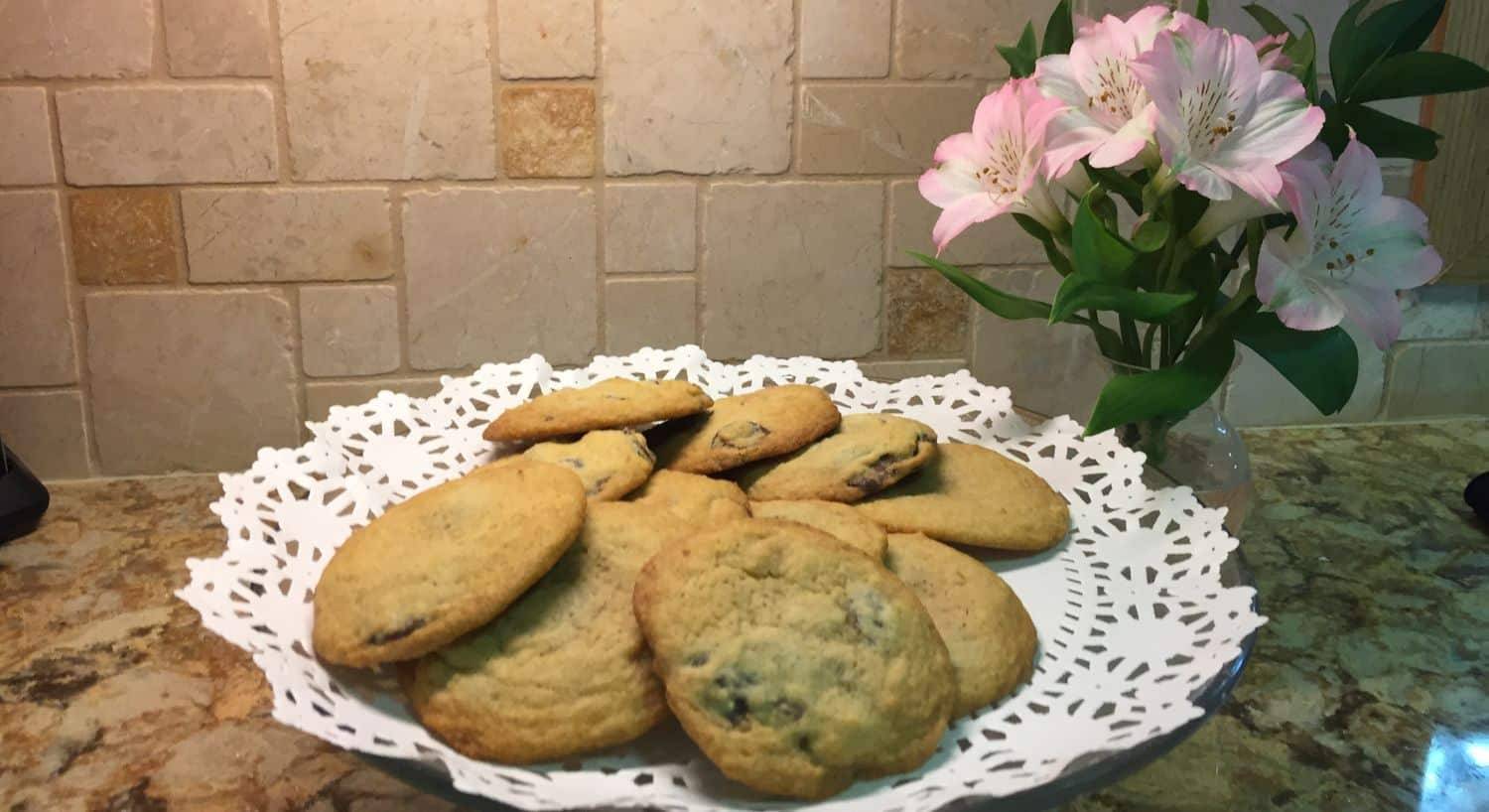 A platter of cookies on a kitchen counter next to a vase of pink flowers