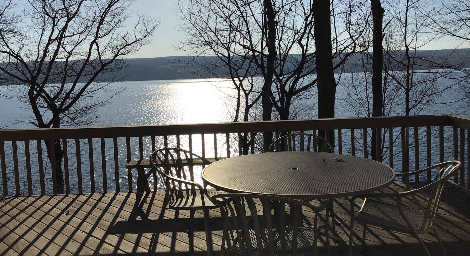 An outdoor deck with round patio table and chairs overlooking an expansive lake