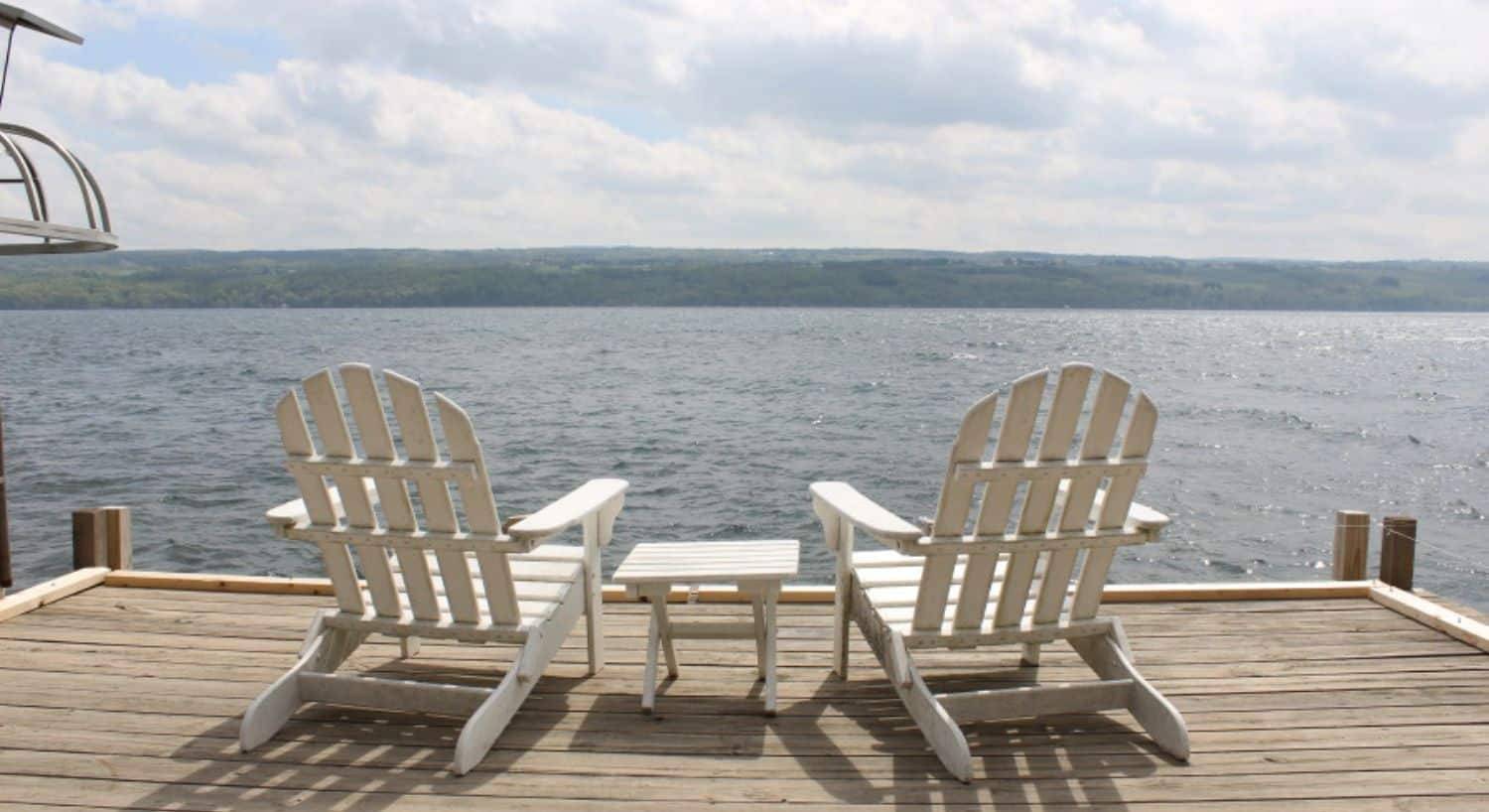 Two white Adirondack chairs at the end of a dock overlooking an expansive lake